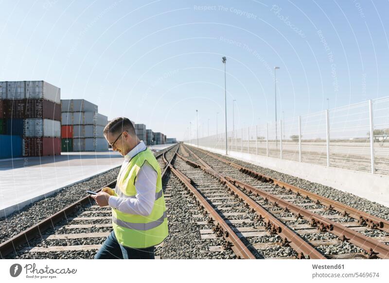 Man on railway tracks in front of cargo containers using cell phone Spain manager managers import white shirt Connection connected Connections connectivity