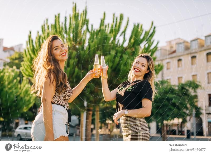 Cheerful female friends toasting beer bottles while standing in city color image colour image Portugal leisure activity leisure activities free time