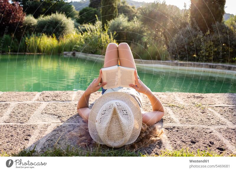 Girl with straw hat lying at swimming pool, reading a book books relax relaxing relaxation enjoy enjoyment indulgence indulging savoring free Liberty free time