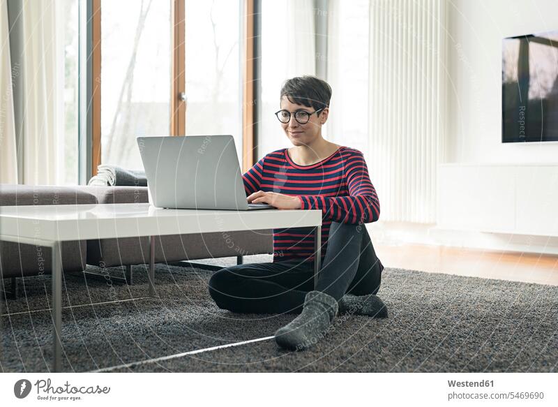 Portrait of woman sitting on the floor of living room using laptop females women Floor Floors Seated Laptop Computers laptops notebook use portrait portraits