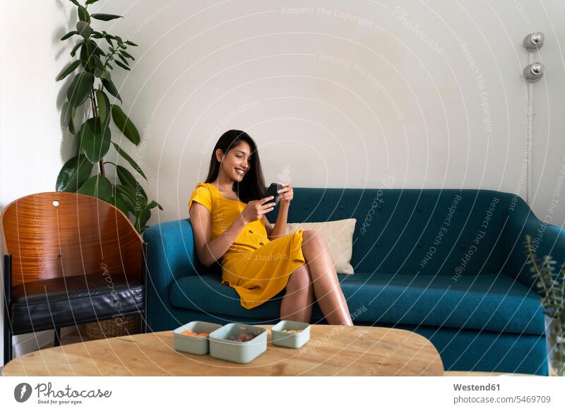Smiling young woman sitting on couch using cell phone human human being human beings humans person persons Indian 1 one person only only one person adult