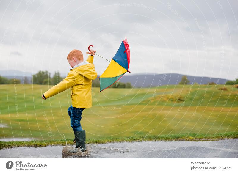Redheaded little boy with umbrella playing in the rain boys males redheaded red hair red hairs red-haired raining child children kid kids people persons