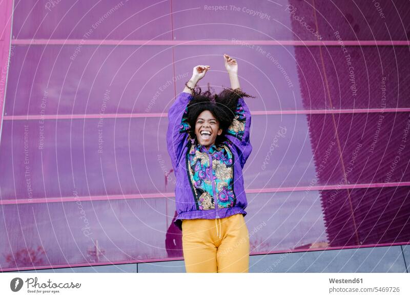Young woman with urban look cheering in front of pink glass wall coat coats jackets exultation jubilate jubilating rejoice rejoicing smile jumps Leaping Ardor