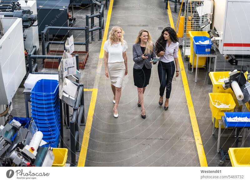 Three women with tablet walking and talking in factory shop floor speaking industrial hall factory hall industrial buildings going factories woman females