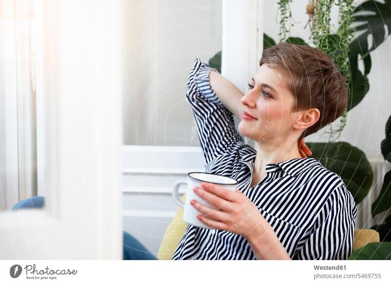 Happy woman sitting relaxed at window, drinking coffee relaxation windows Seated happiness happy Coffee females women relaxing Drink beverages Drinks Beverage