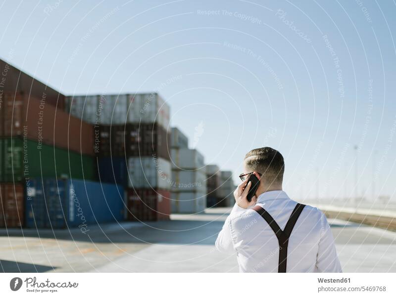 Rear view of manager talking on cell phone in front of cargo containers on industrial site Spain expertise expert knowledge know-how analytic expertise know how