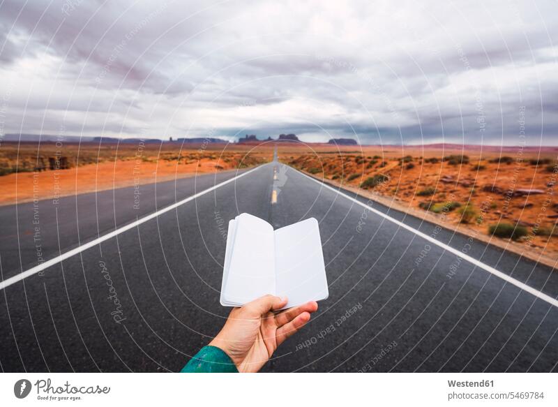 USA, Utah, Hand holding blank notebook over road to Monument Valley diary diaries hand human hand hands human hands young man young men streets roads people