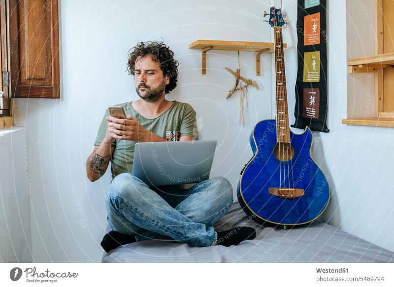Man in his room with mobile phone, laptop and bass guitar Smartphone iPhone Smartphones man men males leisure free time leisure time music Laptop Computers