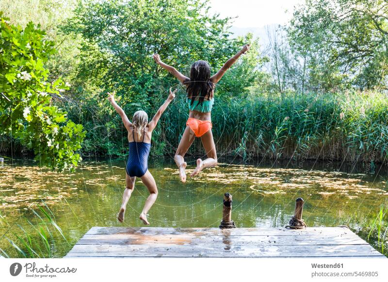 Two carefree girls jumping into pond Pond Ponds females Leaping female friends water waters body of water child children kid kids people persons human being