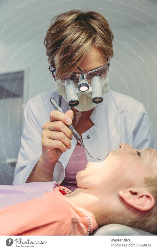 Denist examining boy's teeth, using head magnifiers and dental instrument patient patients headband magnifiers mouth open open mouth checking examine