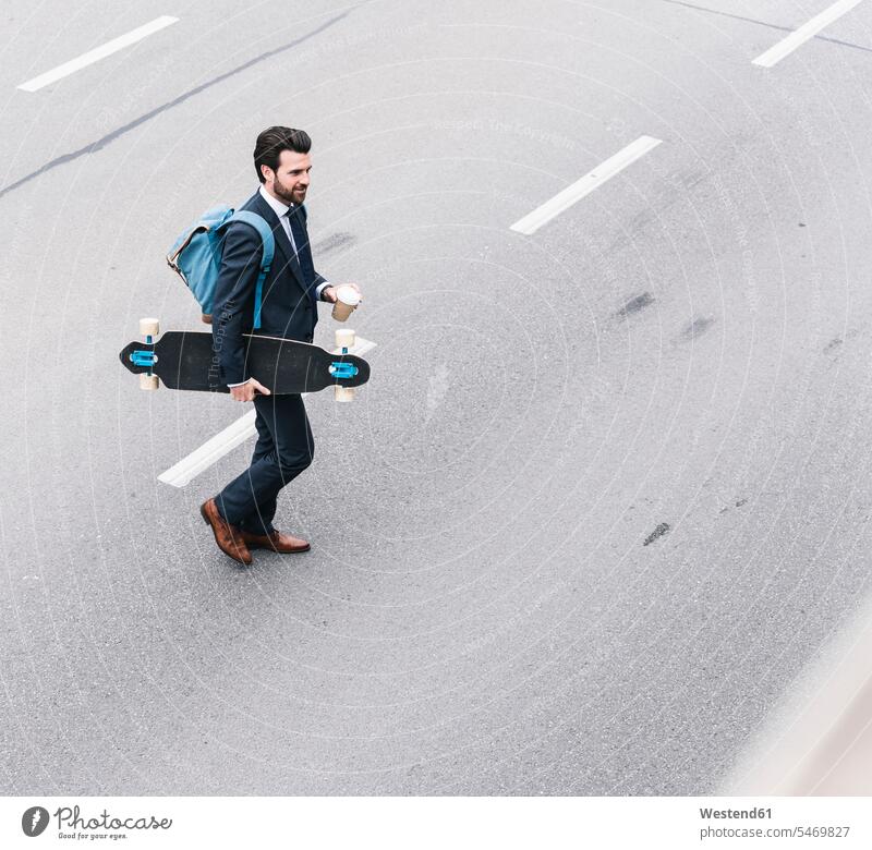 Businessman with takeaway coffee and skateboard walking on the street going road streets roads Business man Businessmen Business men Skate Board skateboards