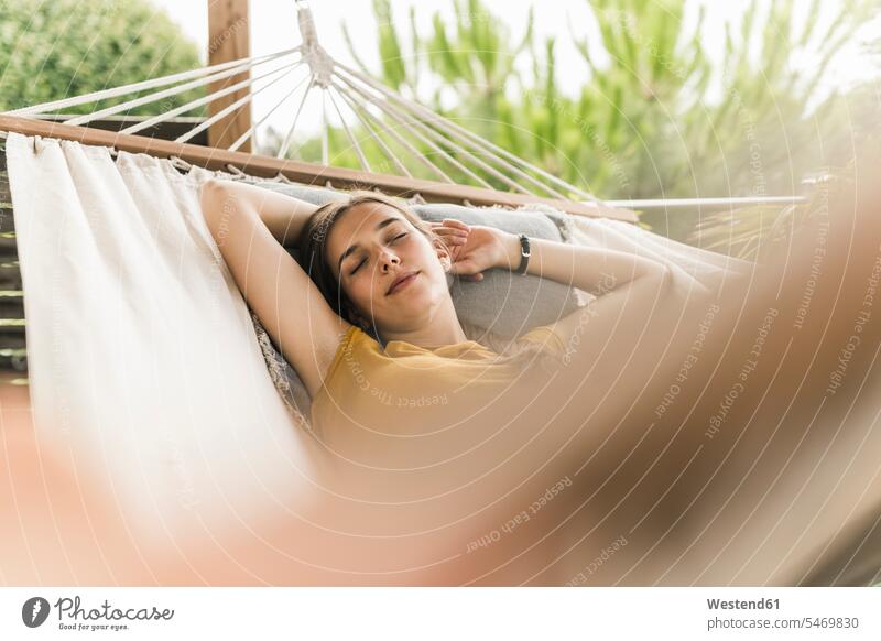 Young woman with arms raised sleeping on hammock in yard color image colour image Germany leisure activity leisure activities free time leisure time