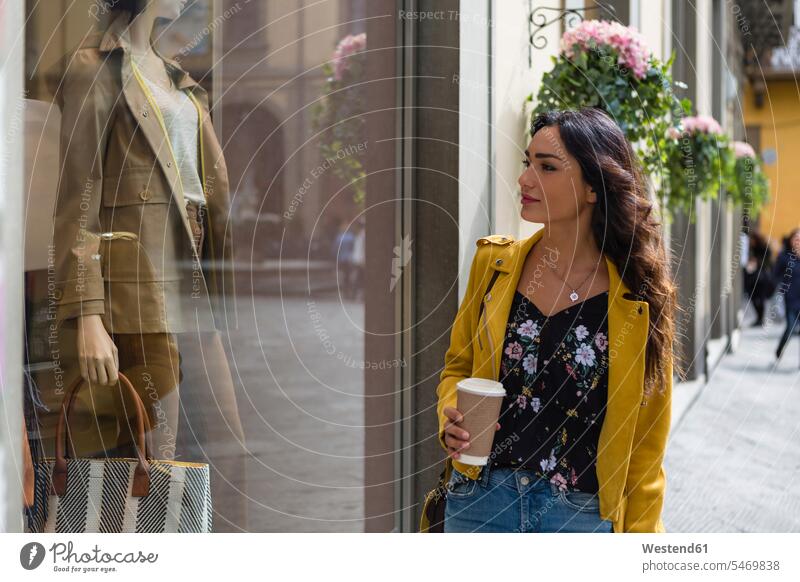 Portrait of young woman wearing yellow leather jacket, holding cup of coffee during shopping Coffee to Go takeaway coffee on the move on the way on the go