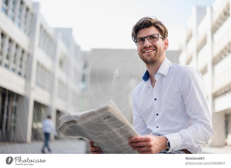 Smiling businessman sitting in the city reading newspaper Seated smiling smile Businessman Business man Businessmen Business men newspapers town cities towns