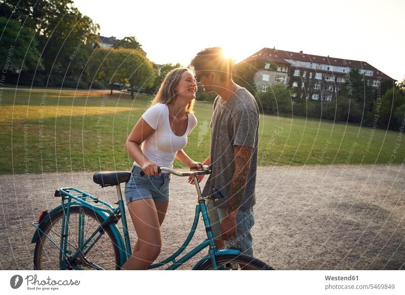 Young woman with bicycle, kissing her boyfriend in park Falling In Love young couple young couples young twosome young twosomes parks adult couple adult couples