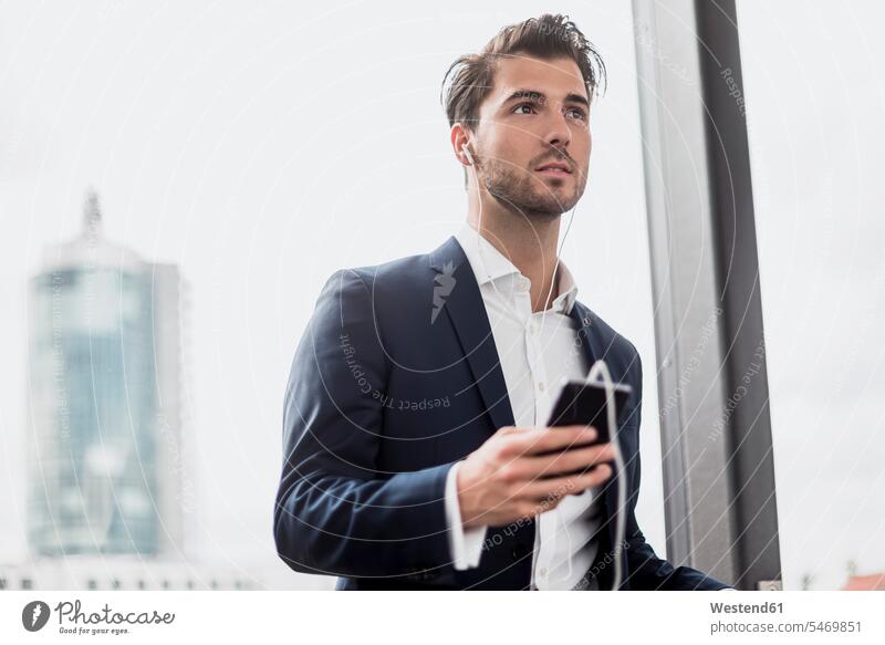 Businessman at the window with cell phone and earbuds Business man Businessmen Business men portrait portraits earphones ear phone ear phones smiling smile