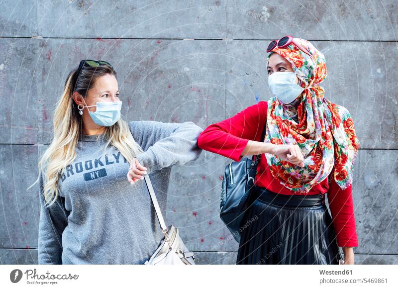 Female friends wearing protective face masks greeting with elbow bumps during COVID-19 color image colour image outdoors location shots outdoor shot