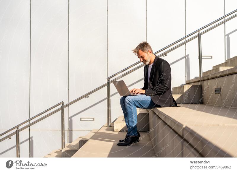 Businessman sitting on steps outdoors using laptop Business man Businessmen Business men Laptop Computers laptops notebook stair Seated use business people