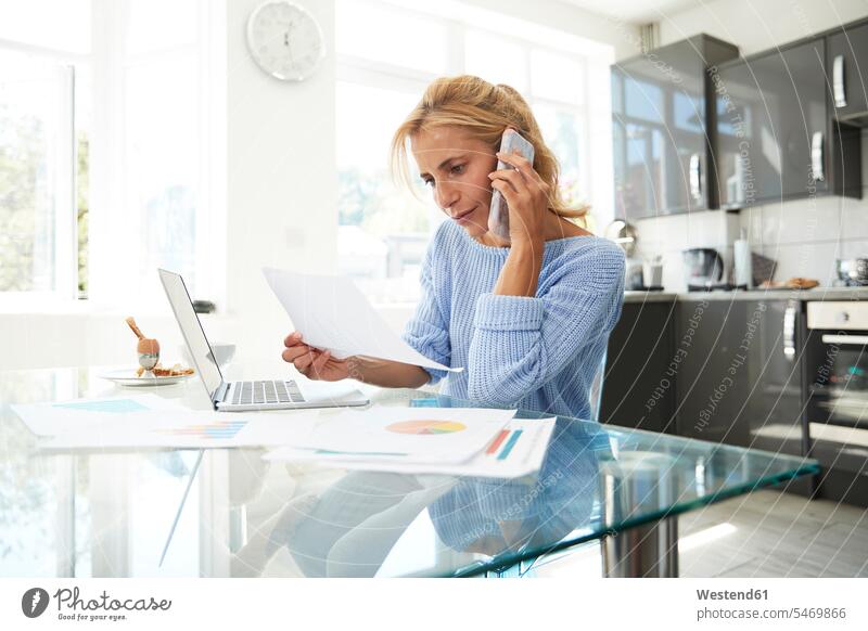 Mature woman talking on phone while in kitchen at home color image colour image indoors indoor shot indoor shots interior interior view Interiors day