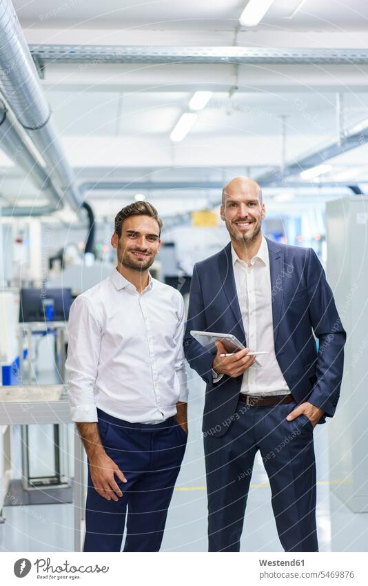 Smiling mature businessman holding digital tablet while standing by young male engineer at factory color image colour image indoors indoor shot indoor shots