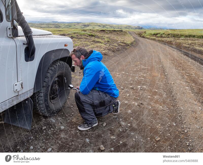 Man kneeling while examining tire pressure through equipment at roadside color image colour image Iceland outdoors location shots outdoor shot outdoor shots day