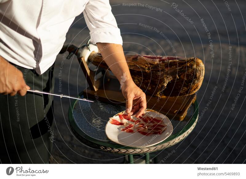Male chef cutting slices of ham on table while standing outdoors color image colour image Spain day daylight shot daylight shots day shots daytime