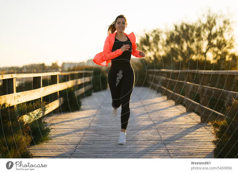 Smiling young woman running on footbridge against clear sky during sunset color image colour image Spain Sportswear Sports Wear Sport Clothes Activewear