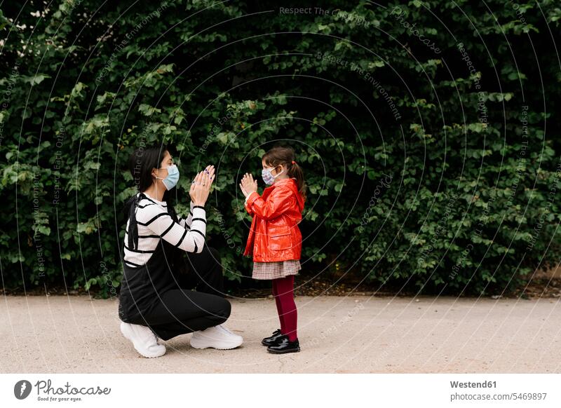 Mother and daughter wearing masks while playing clapping game on street color image colour image outdoors location shots outdoor shot outdoor shots day