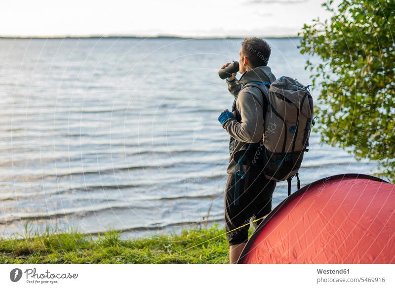 Man camping in Estonia, standing at lake with a backpack, drinking coffee tent tents hiker wanderers hikers Flask nature natural world lakes hiking water waters