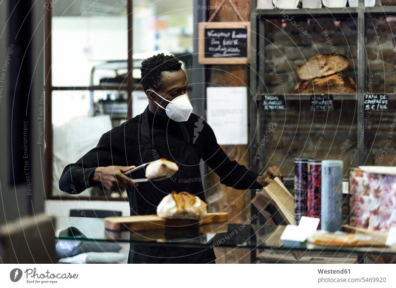 Salesman wearing face mask packing bread while standing at bakery color image colour image outdoors location shots outdoor shot outdoor shots day daylight shot