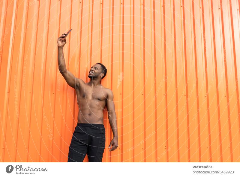 Portrait of athlete taking a selfie in front of an orange wall images picture pictures photo photographs photos telecommunication phones telephone telephones