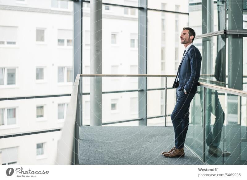 Successful businessman standing in office building, looking out of window, daydreaming offices office room office rooms suit Fullsuit suits full suit leaning