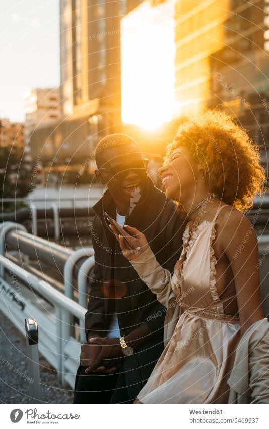 Happy couple with cell phones in the city at sunset town cities towns sunsets sundown mobile phone mobiles mobile phones Cellphone twosomes partnership couples