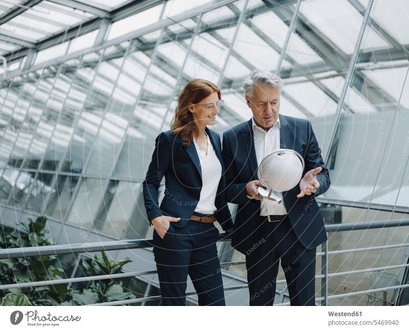 Businessman and businesswoman looking at globe in modern office building human human being human beings humans person persons caucasian appearance