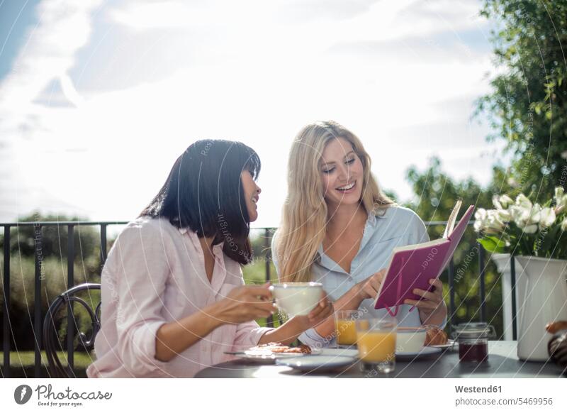 Two women having breakfast at outdoor cafe table, reading book human human being human beings humans person persons Asian Asians caucasian appearance