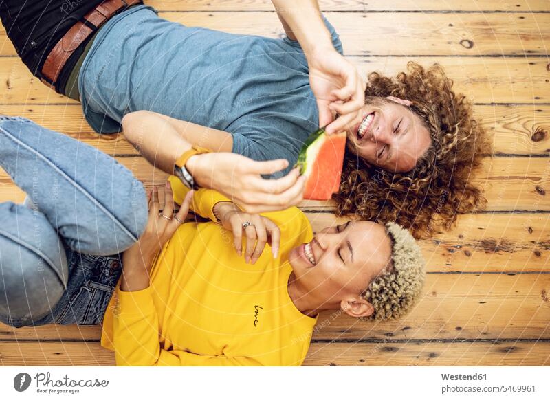 Happy young couple lying on the floor at home sharing a watermelon students relax relaxing hold smile seasons summer time summertime summery Ardor Ardour