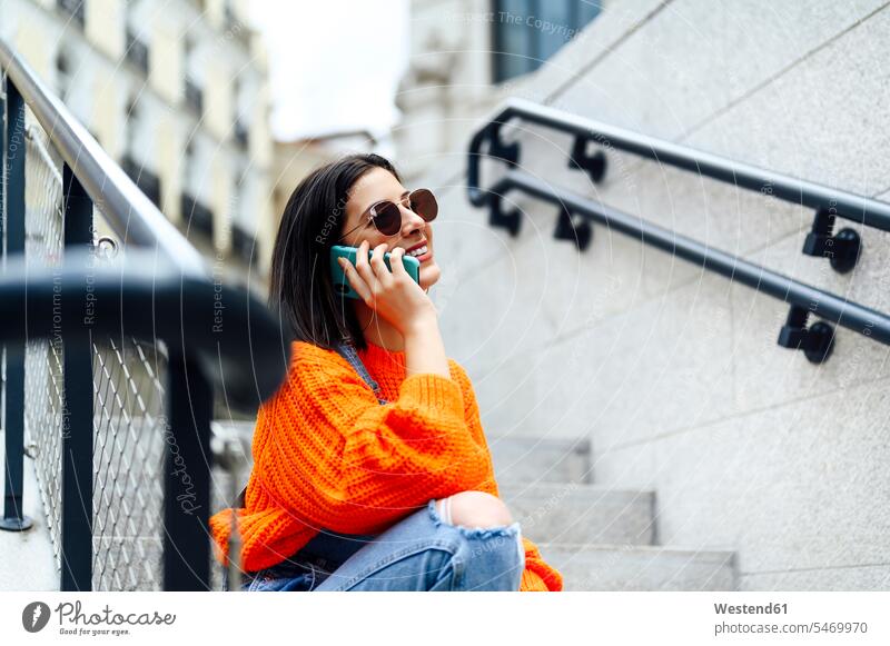 Smiling woman talking on mobile phone while sitting on staircase color image colour image outdoors location shots outdoor shot outdoor shots day daylight shot