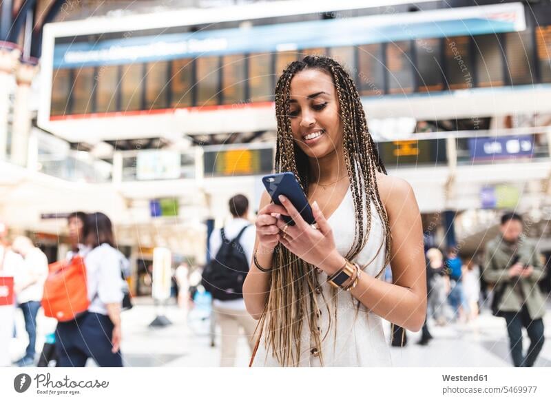 Portrait of happy young woman at train station using smartphone, London, UK human human being human beings humans person persons Mixed Race mixed race ethnicity