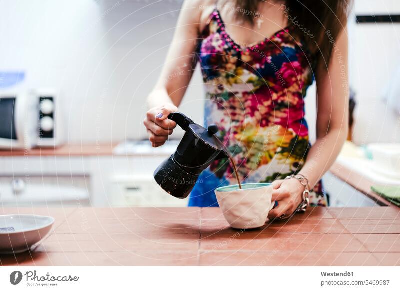 Woman pouring coffee in coffee cup while standing in kitchen at home color image colour image indoors indoor shot indoor shots interior interior view Interiors