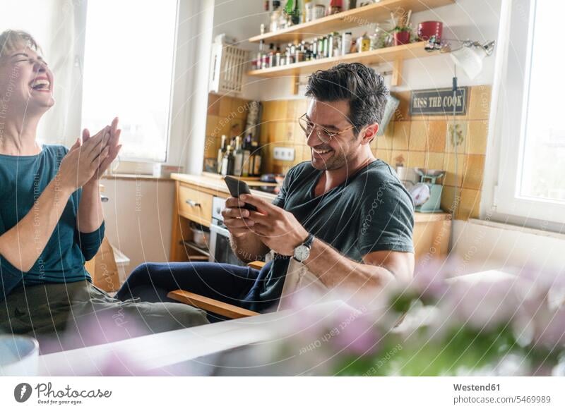 Happy couple sitting at table in kitchen using smartphone windows telecommunication phones telephone telephones cell phone cell phones Cellphone mobile