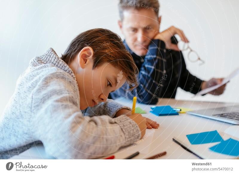 Businessman at desk in office looking at son drawing sitting Seated eyeing sketching offices office room office rooms desks sons manchild manchildren