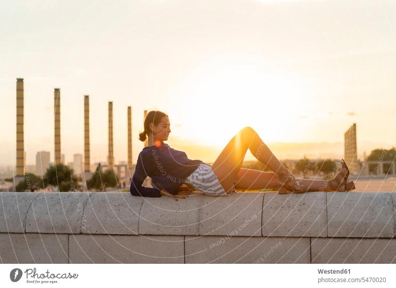 Spain, Barcelona, Montjuic, young woman lying on a wall at sunset walls sunsets sundown females women laying down lie lying down atmosphere atmospheric mood