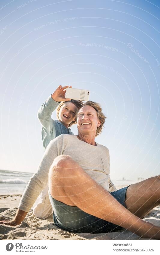 Father having fun with his son on the beach, taking smartphone pictures human human being human beings humans person persons caucasian appearance
