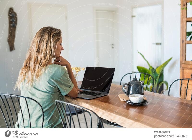 Woman using laptop on dining table at home woman females women Dining Table Dinner Table Dining Tables Laptop Computers laptops notebook Adults grown-ups