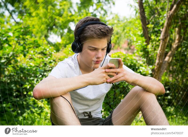 Boy sitting in the garden listening music with headphones and smartphone Smartphone iPhone Smartphones headset hearing gardens domestic garden boy boys males