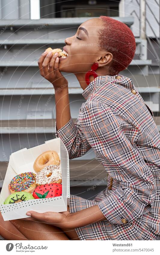 Young woman eating a doughnut from the box human human being human beings humans person persons African black black ethnicity coloured 1 one person only