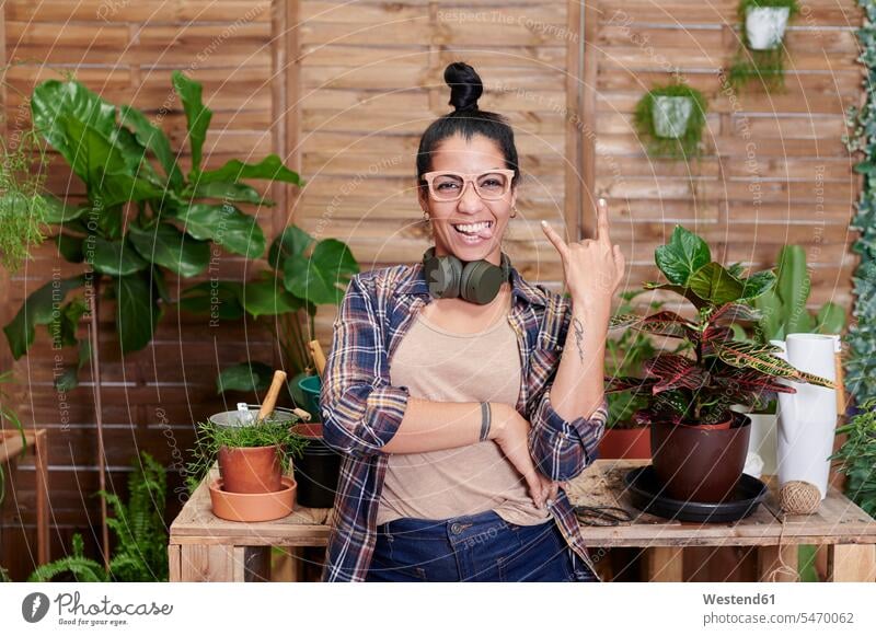 Portrait of a happy young woman gardening on her terrace gardeners flower pot flower pots flowerpots Tables wood wood table headphone headset Eye Glasses