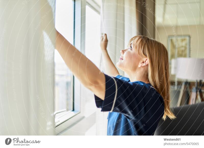Smiling chambermaid opening curtains of window in hotel room color image colour image indoors indoor shot indoor shots interior interior view Interiors
