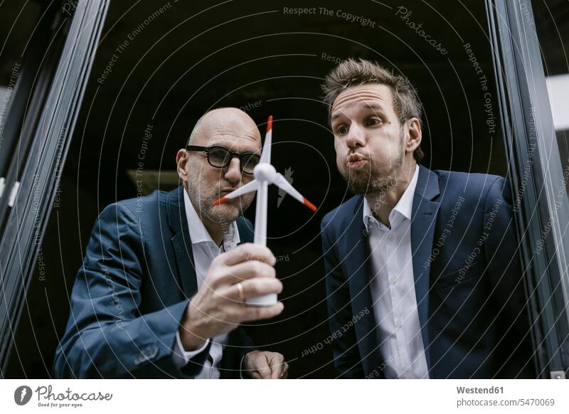 Senior and mid-adult businessman blowing at wind turbine model human human being human beings humans person persons caucasian appearance caucasian ethnicity