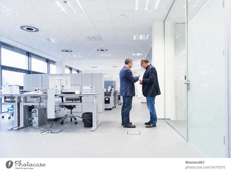 Two businessmen standing in office looking at smartphone colleague Occupation Work job jobs profession professional occupation business life business world